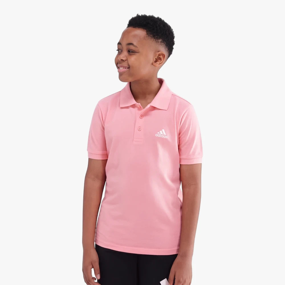 Young boy wearing a pink Adidas short sleeve golfer polo shirt, featuring the white brand logo on the chest.