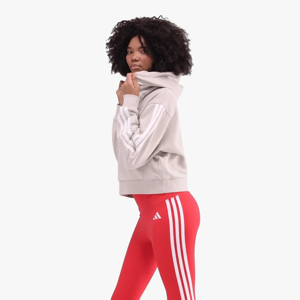 A woman models the beige Adidas S3 Fzl Hz Hoodie with three white stripes on the sleeves and red Adidas leggings with white