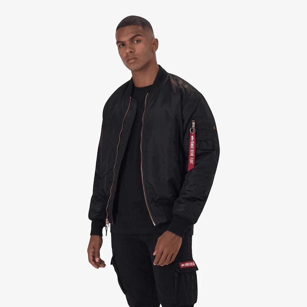 Male model wearing a black Alpha Industries MA-1 Classic bomber jacket over a black t-shirt and black cargo pants, standing.