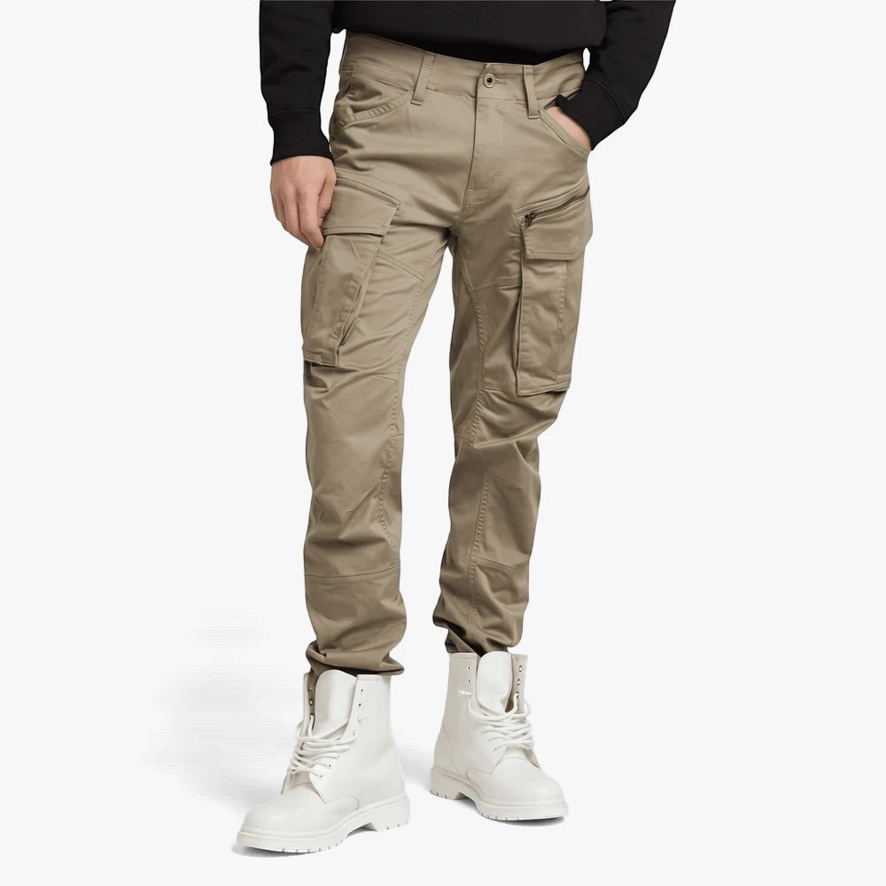A man models G Star Mens Rovic Zip 3D Regular Tapered Cargo Pants in dune, with multiple cargo pockets, paired with white