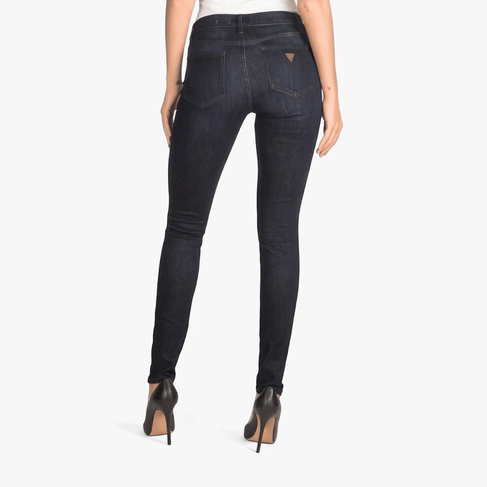 Back view of a model wearing dark blue-black Guess Tina Sexy Curvy Mid Rise Skinny Jeans with black high heels.