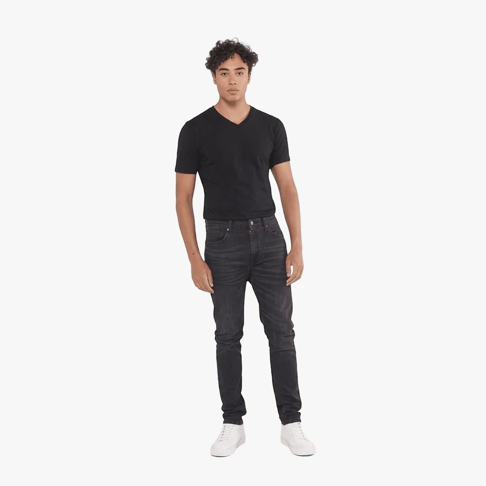 A young man wears black Levis 510 skinny jeans, a black v-neck t-shirt, and white sneakers, standing full-body in a studio