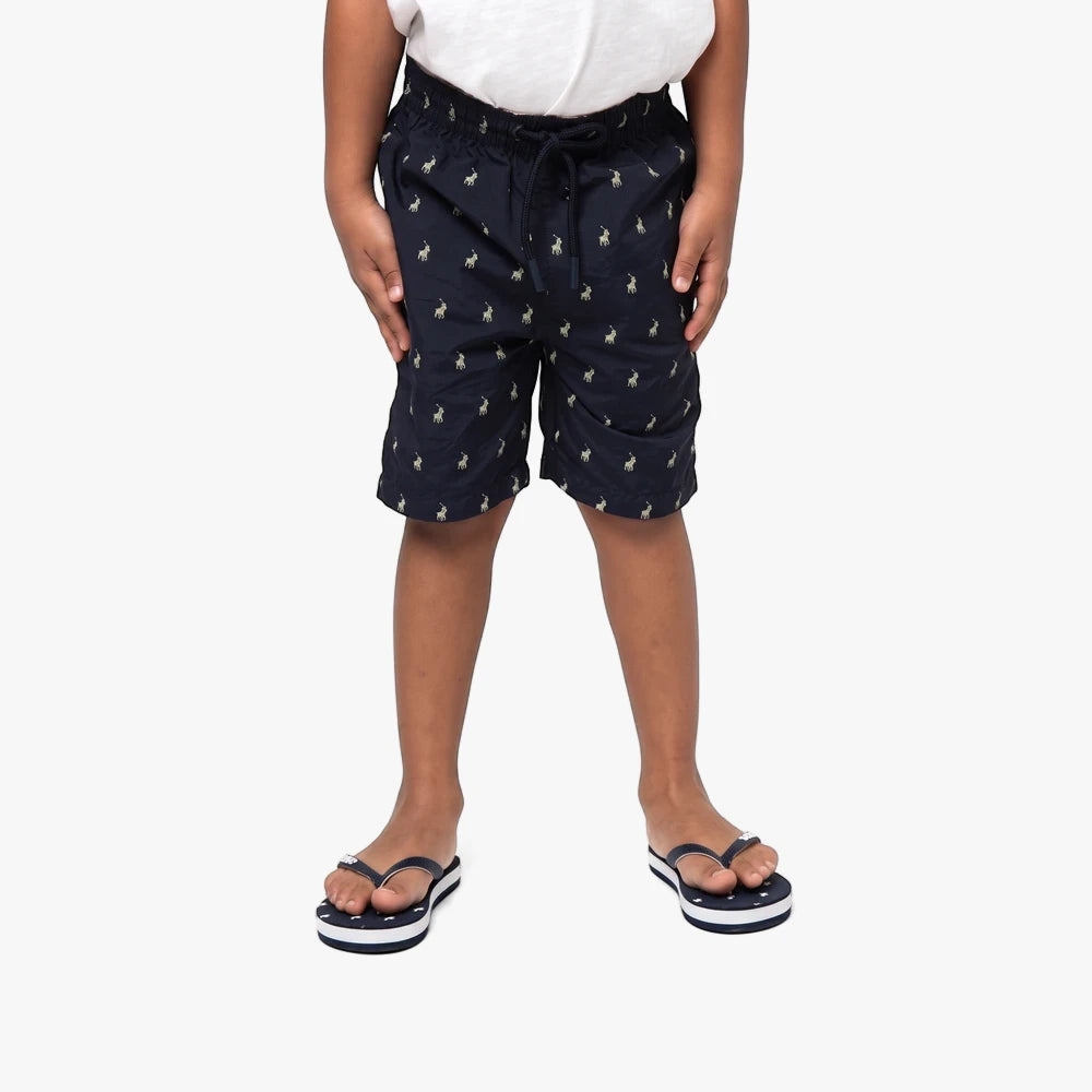 Polo Boys Bradley Monogram Beach Shorts in navy with a repeating monogram pattern, worn with striped flip-flops.