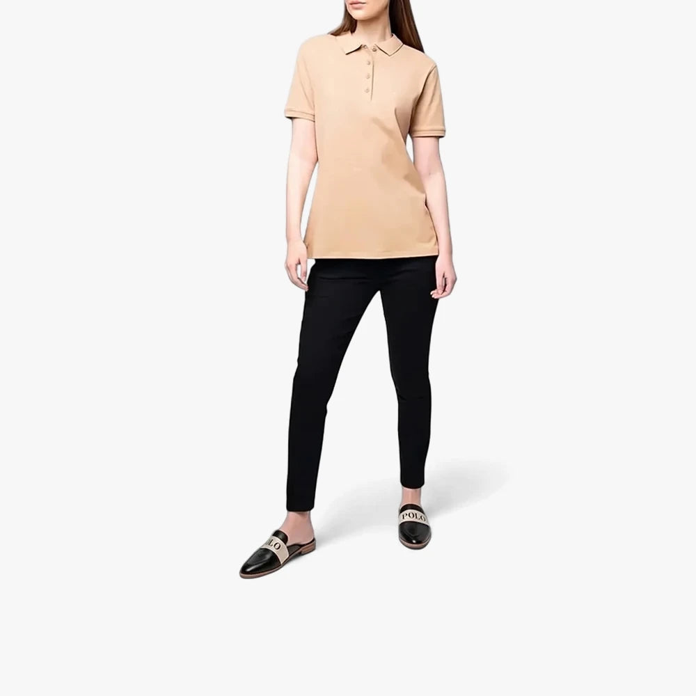 A woman models a taupe Polo Margot short sleeve golfer, paired with black pants and black slip-on shoes.