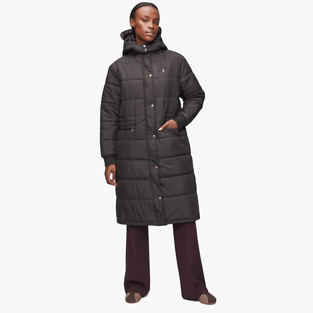 A female model wears a long black quilted Polo Mia puffer jacket with a hood, styled with dark pants and slip-on shoes.