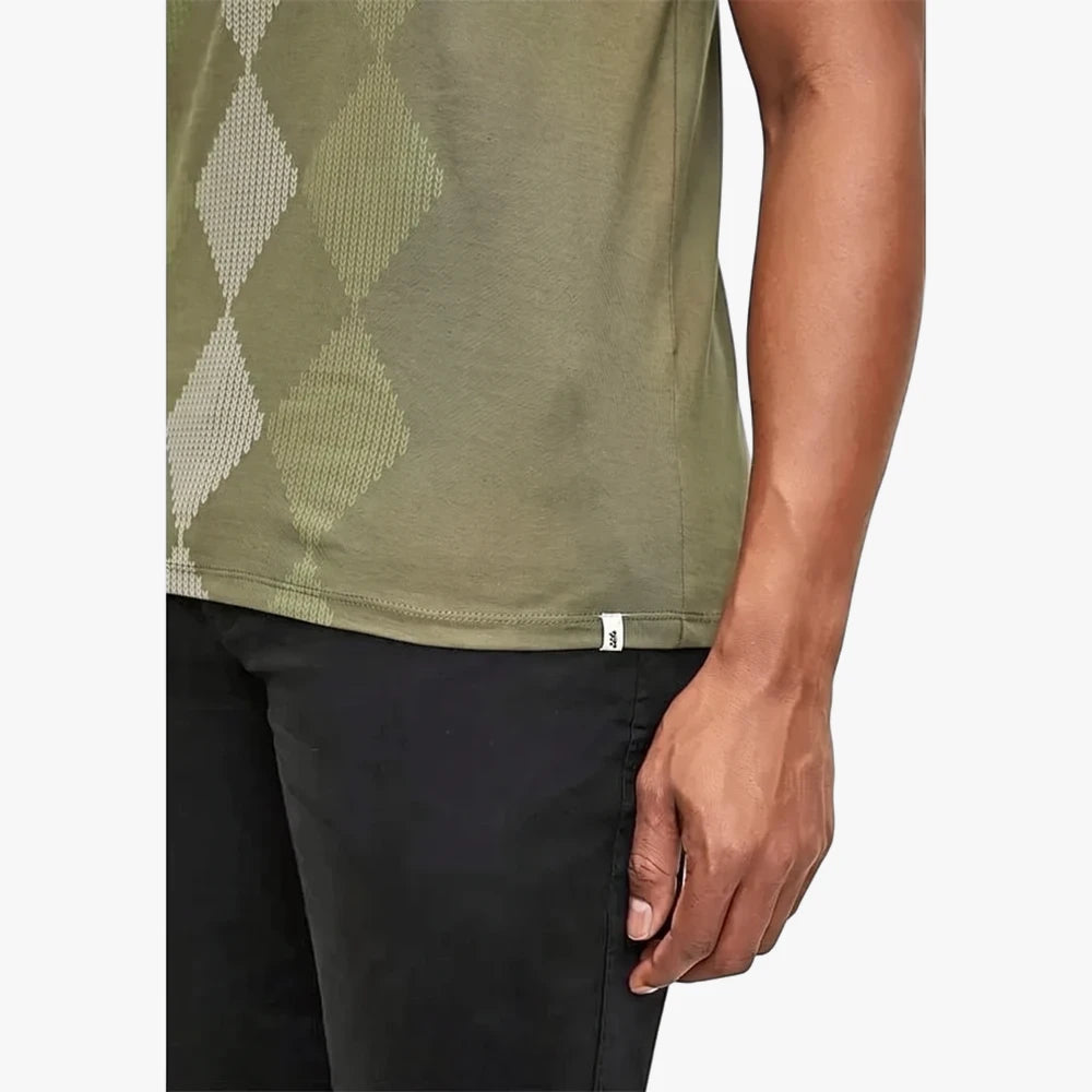 Close-up of a man wearing a fatigue green Pringle Hugo short sleeve tee with an argyle pattern and black pants.