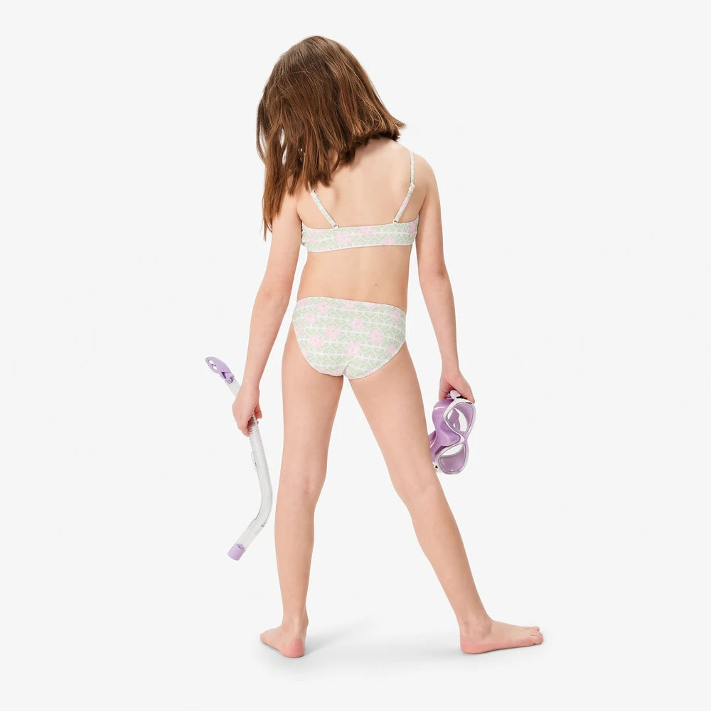Young girl wearing a Roxy Fairy Beach Flutter Set two-piece swimsuit in light green with pink hibiscus floral pattern,