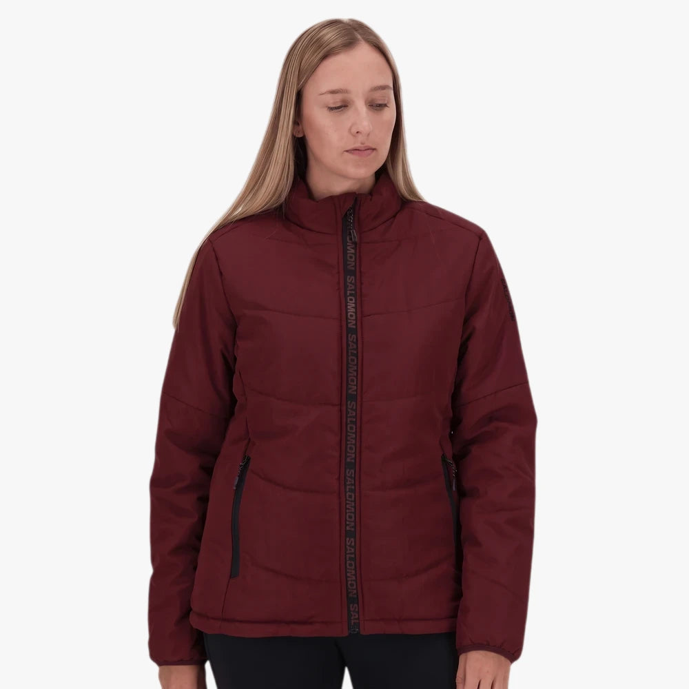 Woman models a Salomon Womens Cove Jacket in cherry liqueur, a maroon puffer jacket with black zippers.