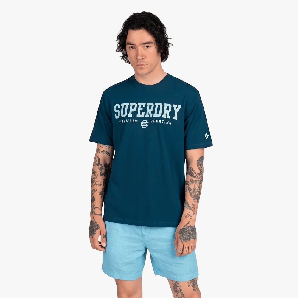 Male model wearing a blue Superdry Core Sport short sleeve tee and light blue shorts, standing against a white background.