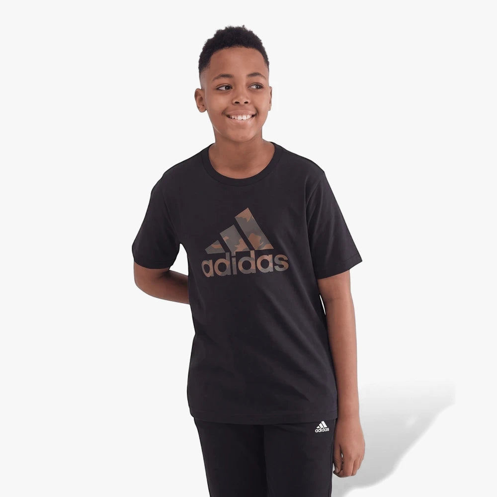 Young boy wearing a black Adidas short sleeve t-shirt with a camouflage logo and black pants, smiling and standing.