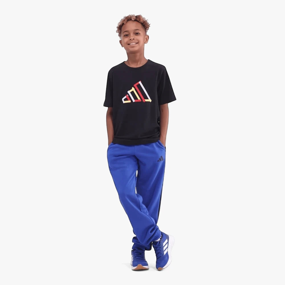 A young boy wearing a black Adidas Table Tech short sleeve tee, blue sweatpants, and blue sneakers, standing with hands in