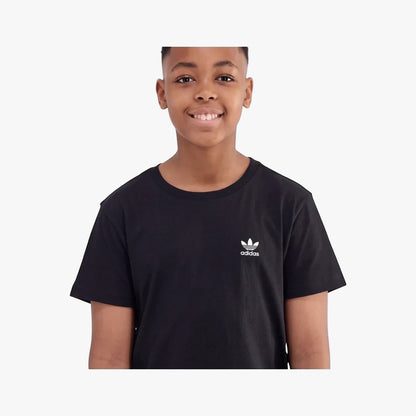 Young boy smiling in an Adidas Youth Ess Short Sleeve Tee in black, showcasing the white trefoil logo on the chest.