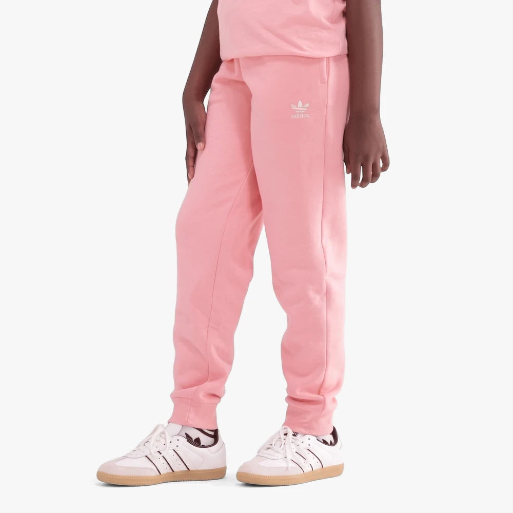 Lower body view of a child wearing pink Adidas girls track pants with a white trefoil logo and white sneakers with brown
