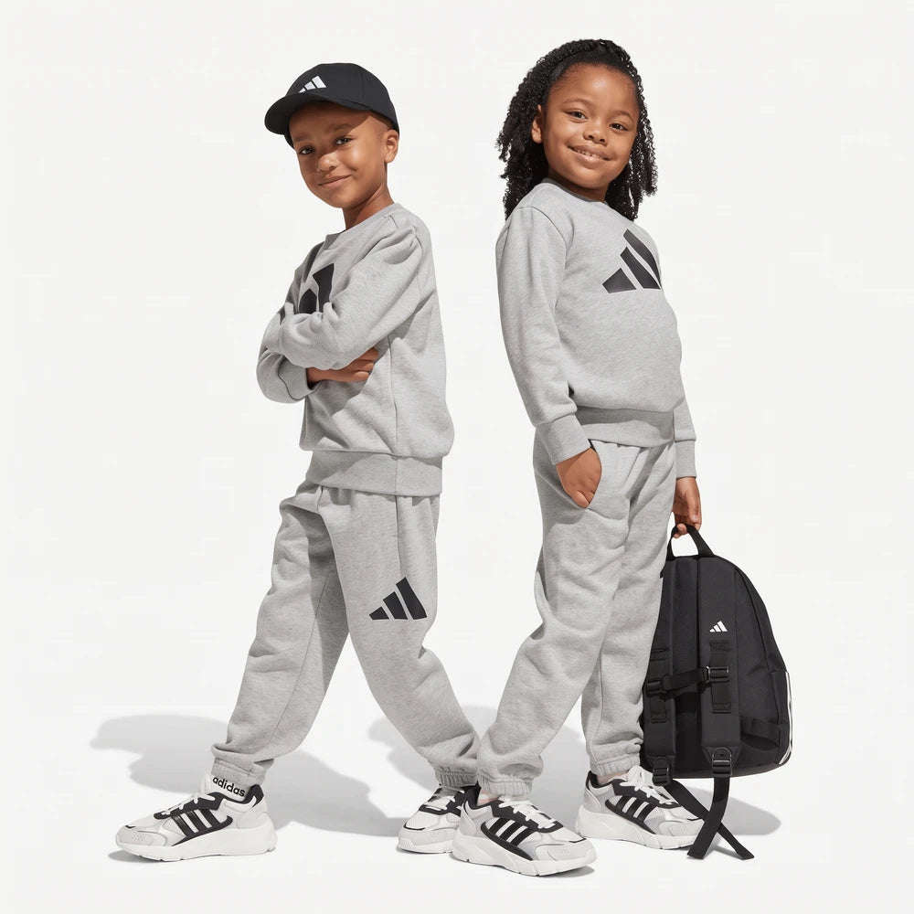 Two children, a boy and a girl, wearing gray Adidas Bl Ft sweatpants and matching sweatshirts, posing with a black backpack