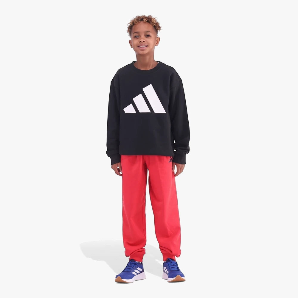 Young boy in a black Adidas sweatshirt and ruby red Adidas Kids Blend Fleece sweatpants with blue sneakers.