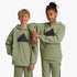 Two children wearing matching olive green Adidas Future Icons Logo Hoodies with black logos and track pants.