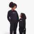 Two young girls wearing black Adidas Kids Lin Ft Crew Sweaters and matching track pants with white stripes, smiling
