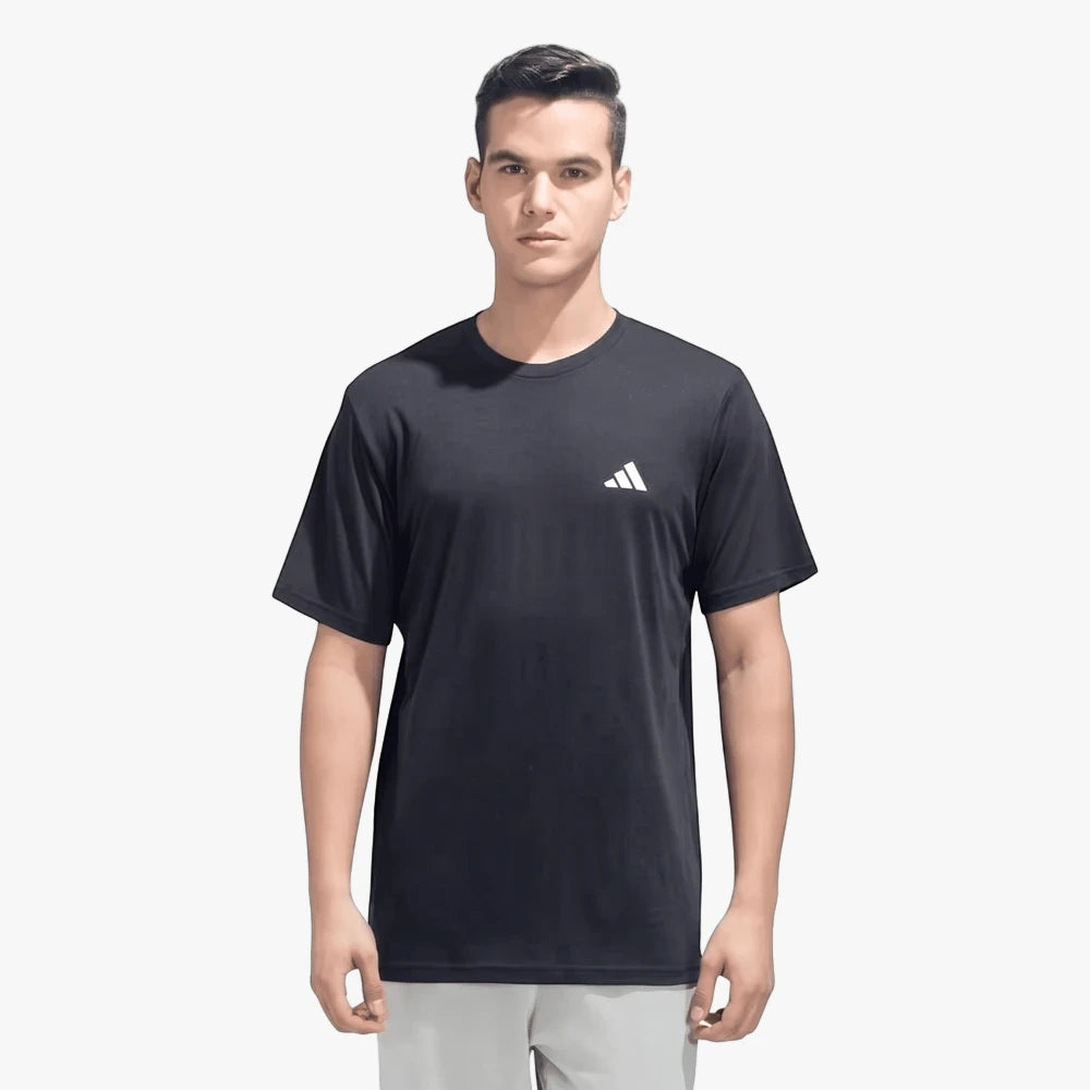 A male model wears a black Adidas Train Essentials short sleeve tee, featuring a white logo, paired with light grey shorts,