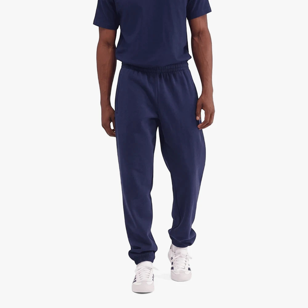 Adidas Mens Trefoil Essentials French Terry Joggers in Night Indigo, worn by a man with a navy t-shirt and white sneakers.
