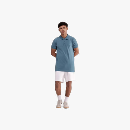 Adidas Mens Trefoil Essentials Polo Tee in blue, worn by a male model standing in white shorts and sneakers.