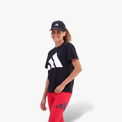 A smiling woman models an Adidas black t-shirt with a large white logo, red leggings, and a black cap in activewear.