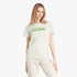 A woman wears an Adidas Womens Doodle Short Sleeve Tee in linen green, featuring a distinctive green doodle Adidas logo on
