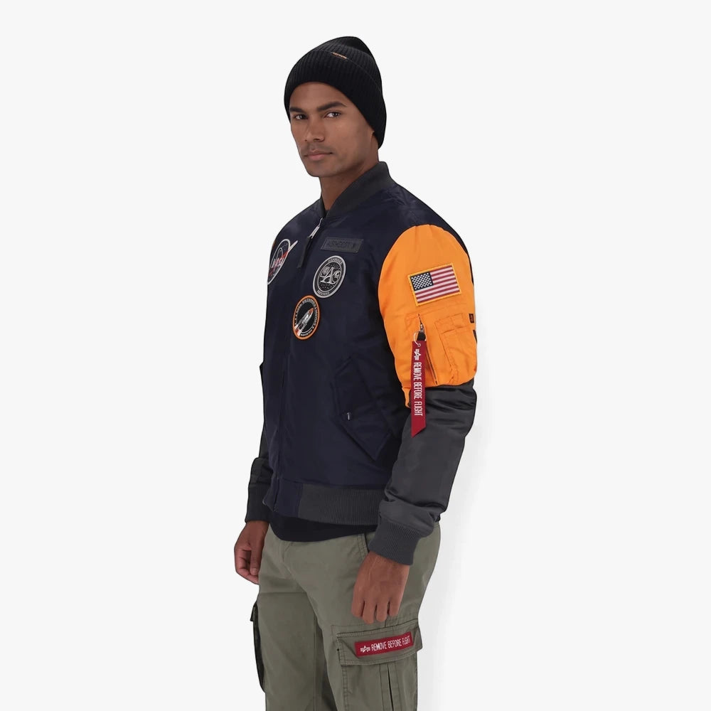 Male model wearing a navy and orange Alpha Industries Nasa Hornet Jacket with various patches, a black beanie, and green