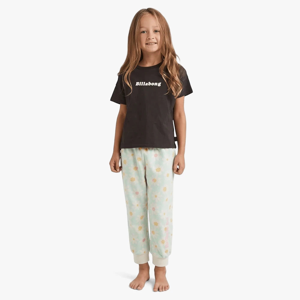Young girl wearing a black Billabong short sleeve tee and mint green floral print sweatpants, standing barefoot.