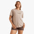 A woman models a Billabong Womens Emerald Island Short Sleeve Tee in cobblestone, paired with dark shorts, on a white