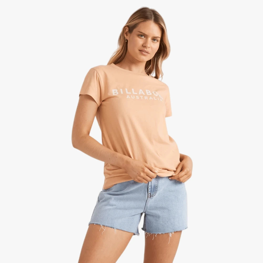 Woman models a Billabong Society short sleeve t-shirt in baked clay, paired with light blue denim shorts.