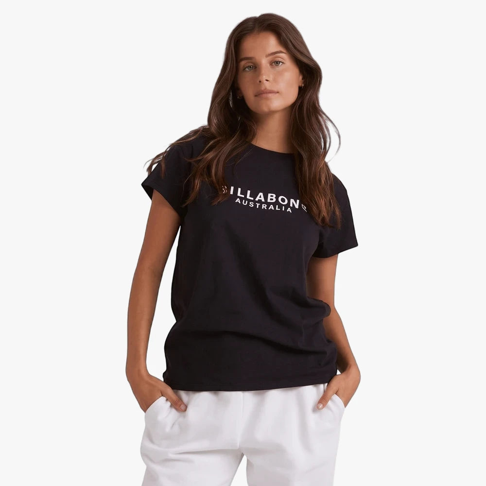 Billabong Womens Society Short Sleeve Tee in black, worn by a woman with long brown hair, standing with hands in pockets.