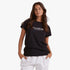 Billabong Womens Society Short Sleeve Tee in black, worn by a woman with long brown hair, standing with hands in pockets.