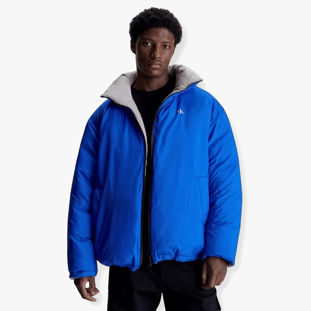 Man wearing a Calvin Klein Mens Reversible 90S Puffer Jacket in blue and grey, front view.