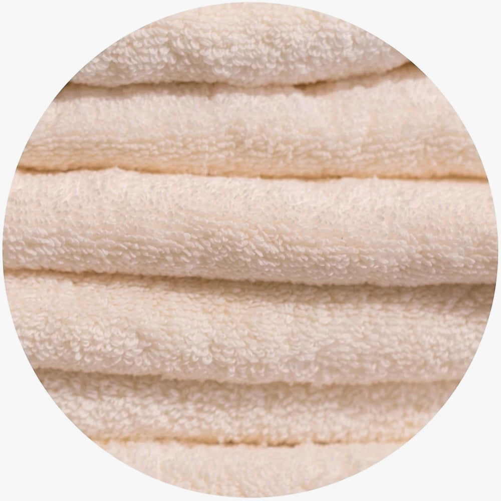 Close-up of fluffy beige Colibri Imperial Zerotwist bath sheets stacked horizontally, showcasing the soft terrycloth texture.