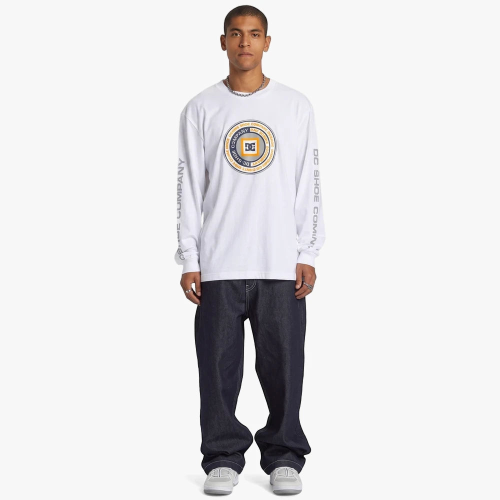 Dc Mens Throwback Long Sleeve Tee in white, featuring a circular chest graphic and worn with baggy dark denim jeans.