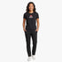 A woman wears a black Diesel Womens Just Small New D Logo Tee and black pants, showcasing the shirt&