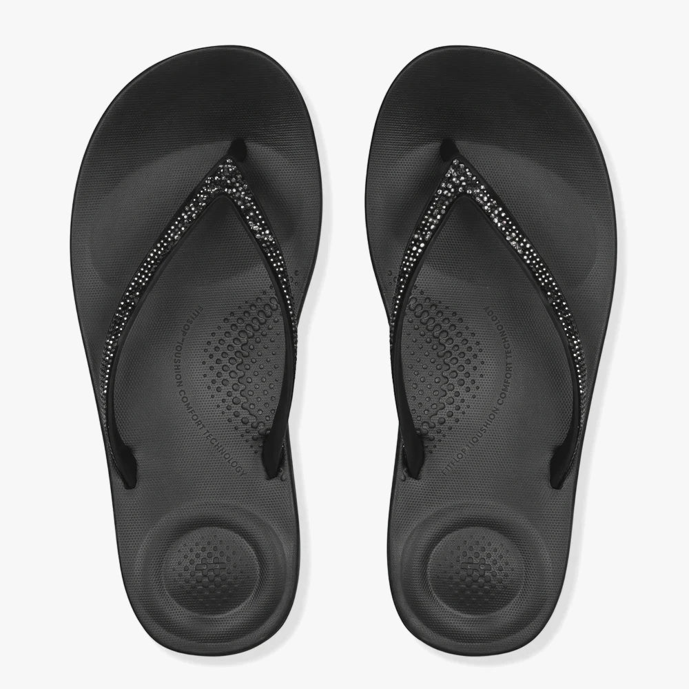 A top-down view of a pair of black Fit Flop I Qushion Sparkle Sandals with glittering rhinestone straps on the vamps.