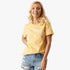 Blonde woman smiling, wearing a yellow Fox Racing Arch short sleeve tee and distressed denim shorts.