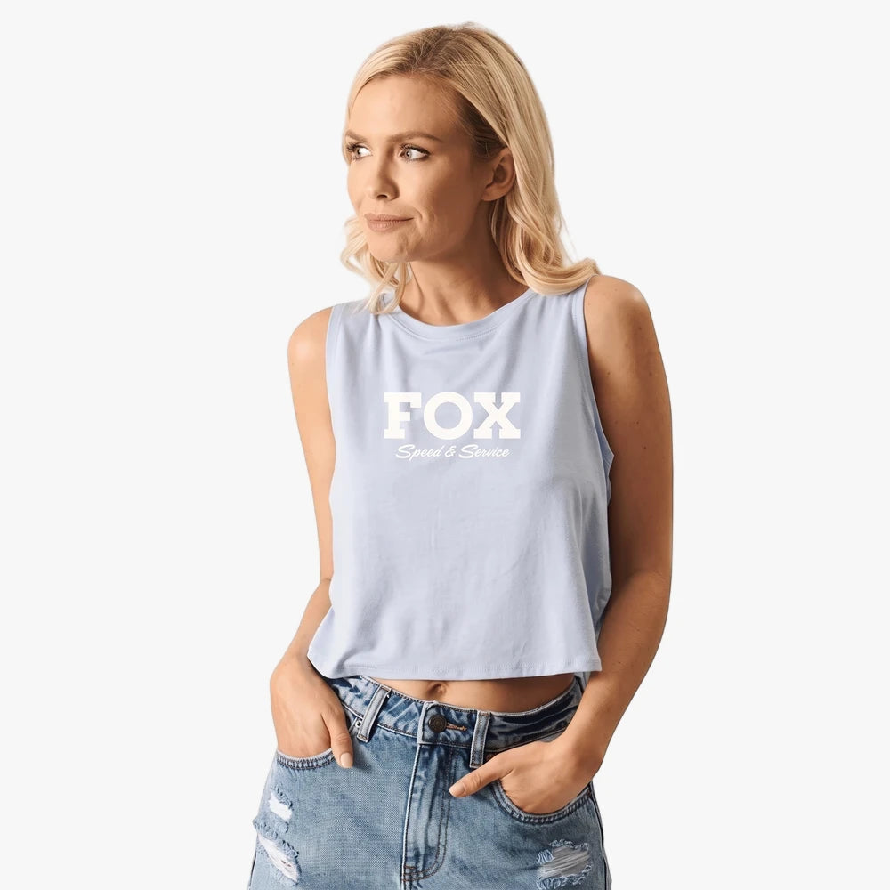 A blonde woman wearing a light blue Fox Womens Speed Crop Tank Tulip and distressed blue jeans, posing against a white