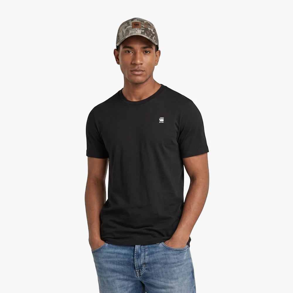 Man wearing a black G Star Basic Short Sleeve Tee, blue jeans, and a camouflage cap, posing with hands in pockets.