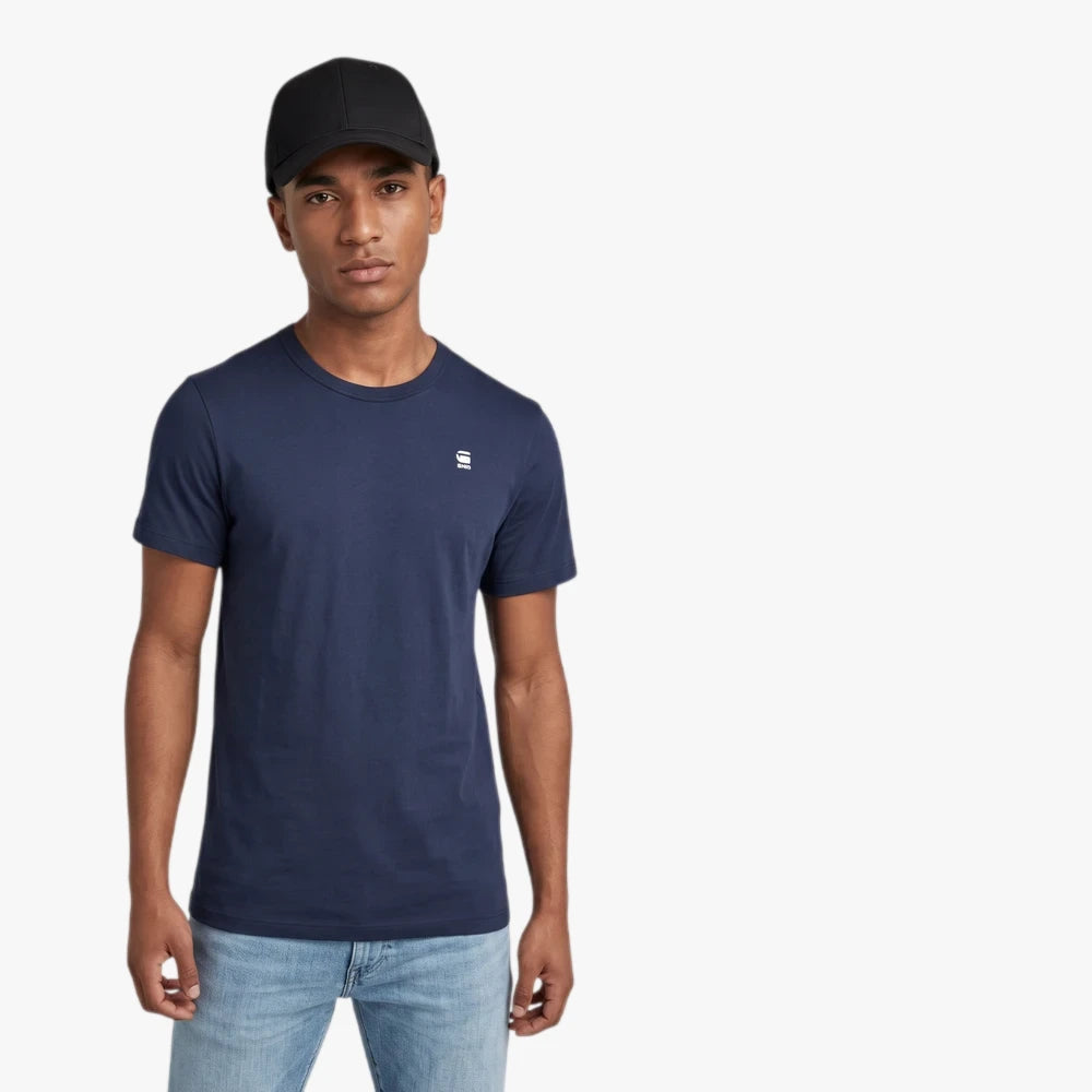 Male model wearing a navy G Star Basic Short Sleeve Tee, light wash jeans, and a black baseball cap.