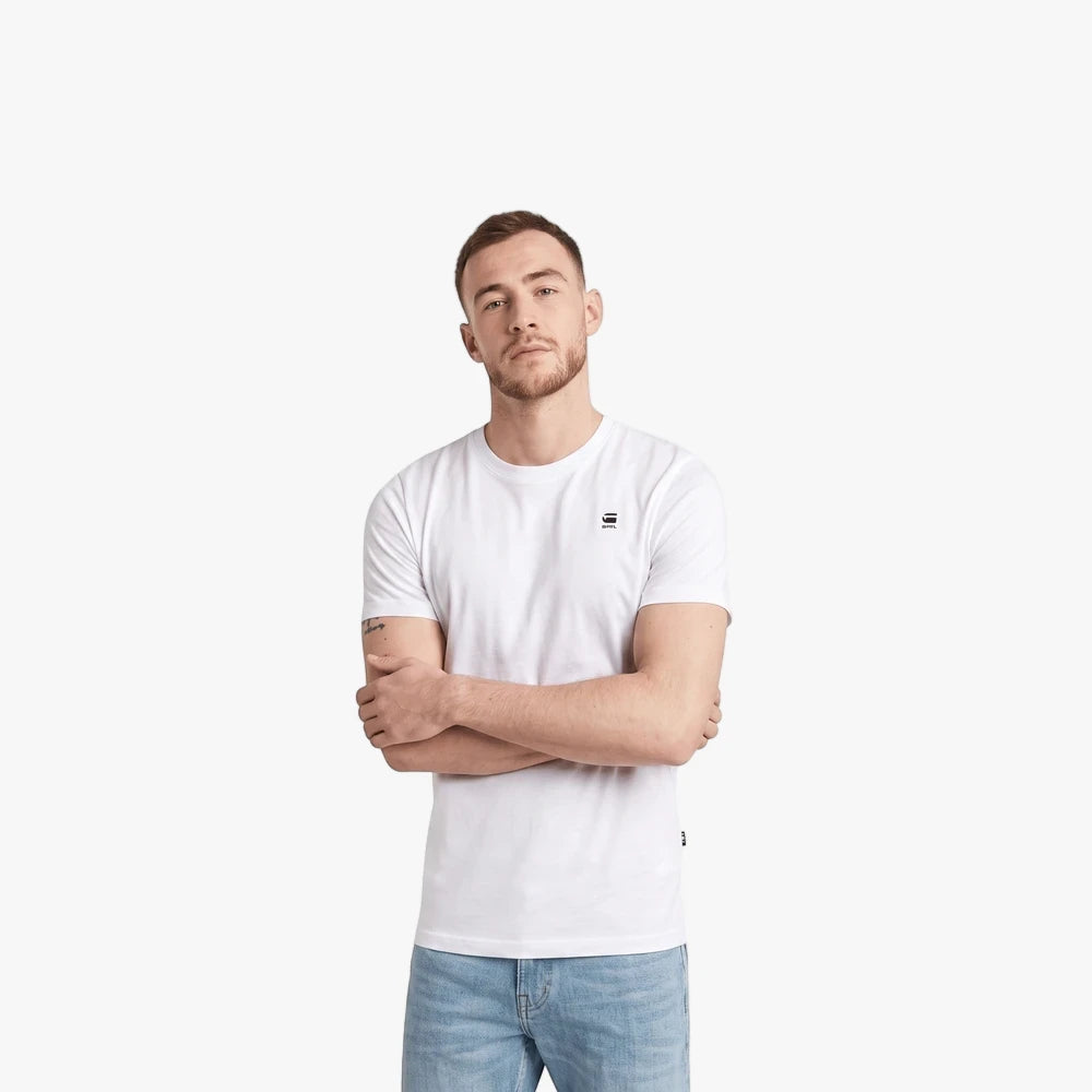 A man models the G Star Mens Basic Short Sleeve Tee in white, paired with light blue jeans. He stands with arms crossed,