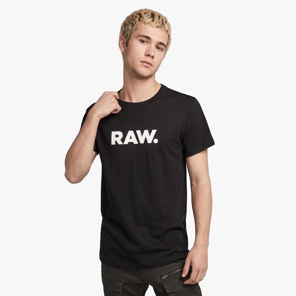 Young man wearing a black G Star Holorn short sleeve tee with a RAW. logo and dark jeans, standing against a white