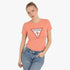 A woman models a coral Guess Womens Original Triangle short sleeve tee. She wears blue denim jeans and poses against a clean