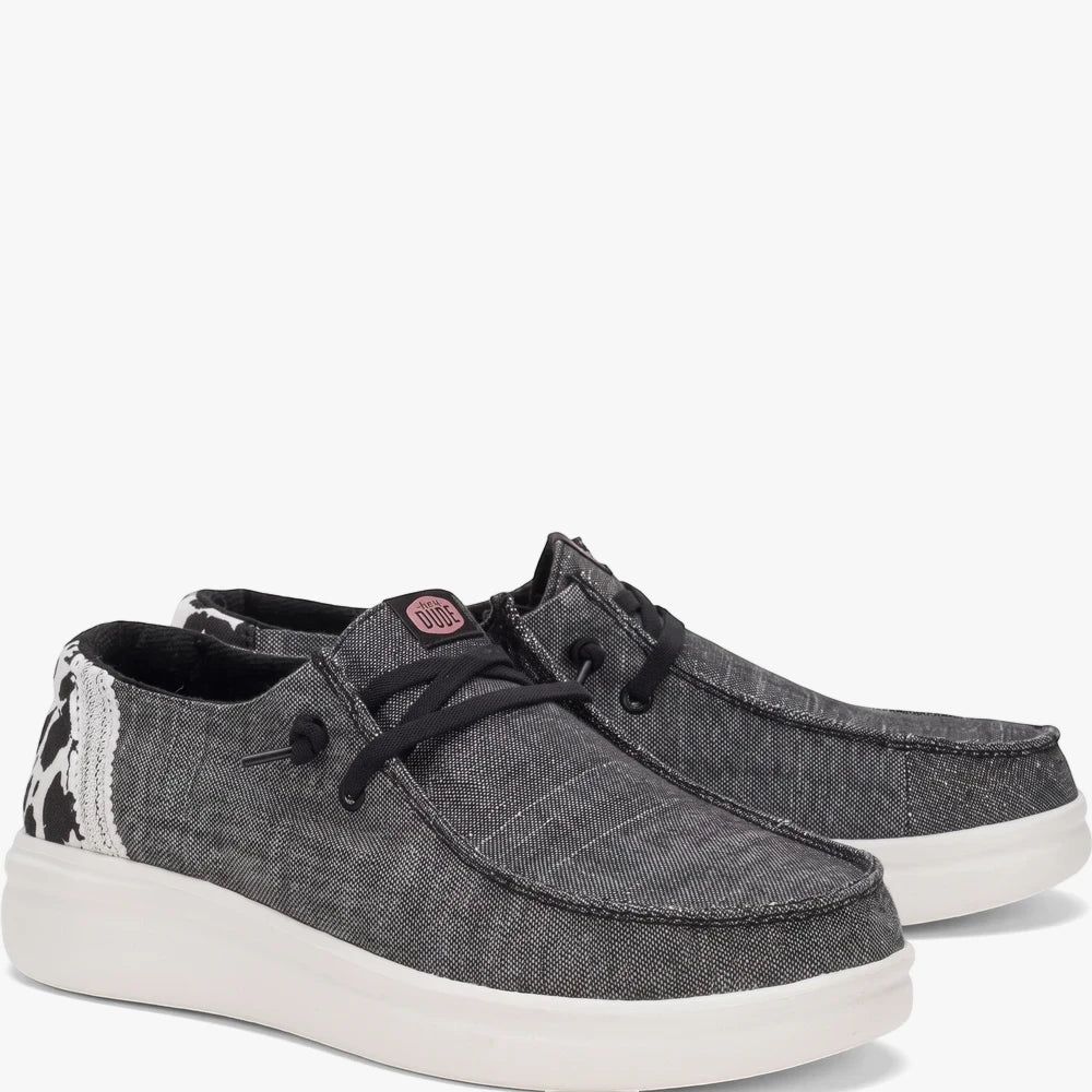 A pair of Hey Dude Womens Wendy Rise Animal Black Multi casual shoes, featuring dark gray canvas uppers, cow print heel, and