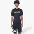 Male model wearing a black Hurley Oao Quickdry short sleeve rashguard and black shorts with white stripes, standing upright.