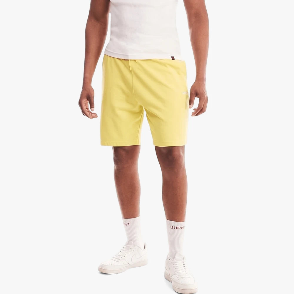 Man wearing yellow Levis Mens Sweat Shorts with a white tank top and white sneakers, standing on a white background.