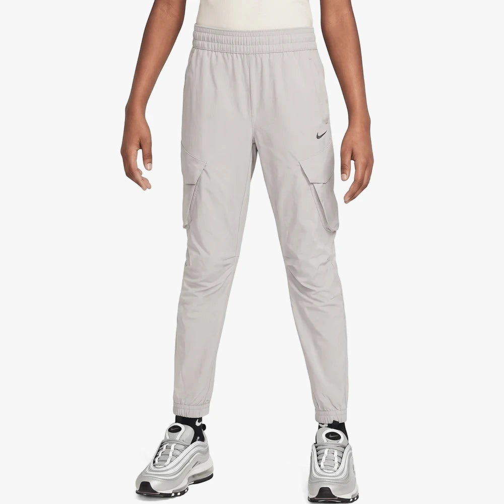 Nike Boys City Utility Cargo Pants in light grey, featuring cargo pockets, an elastic waistband, and tapered fit, shown on a