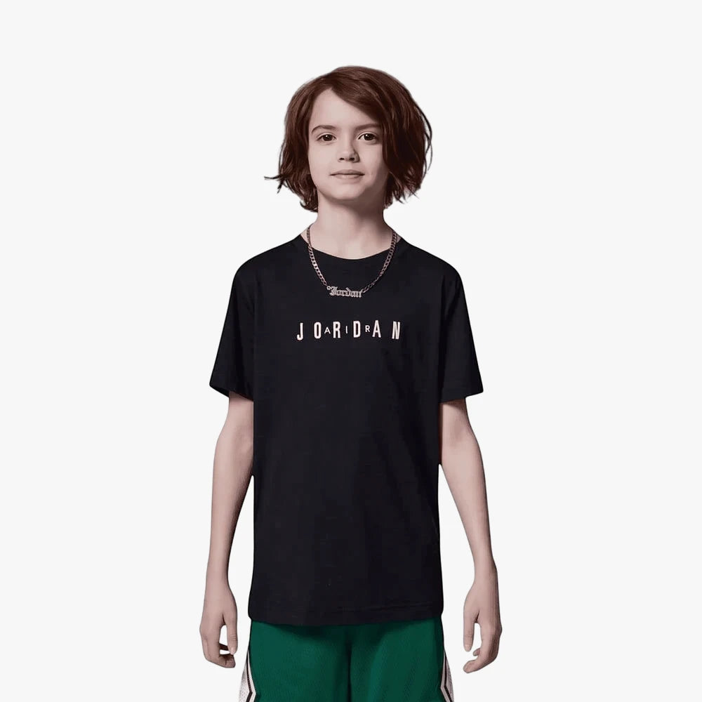 A young boy wears a black Nike Jdb Mj Wordmark Emb Crew short sleeve tee with white text and green shorts.