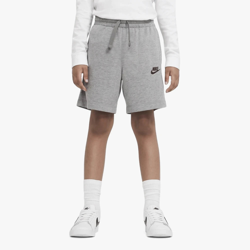 Grey Nike Boys Jersey Shorts with a drawstring waist, worn by a child, paired with a white long-sleeve top and white